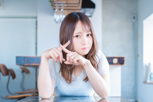 指で×ポーズをする若い女性の写真