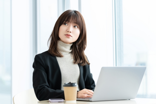 パソコンの前で斜め上を見上げる若い女性の写真